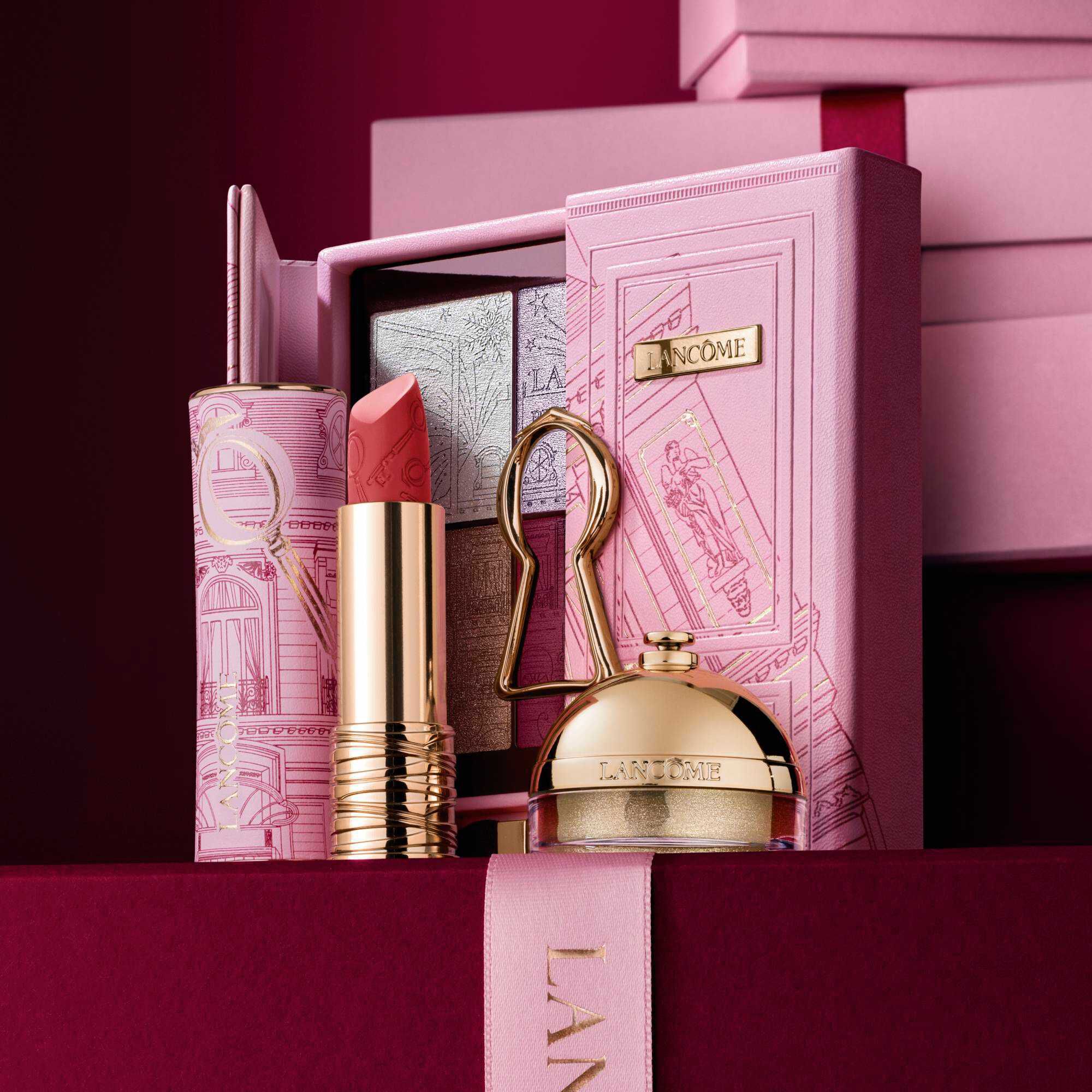 Image of Lipstick Drama matte limited edition, Ring & Shine & The Suite Escape Palette standing in front of a pile of pink and dark red gift boxes, set against a dark red background. 	