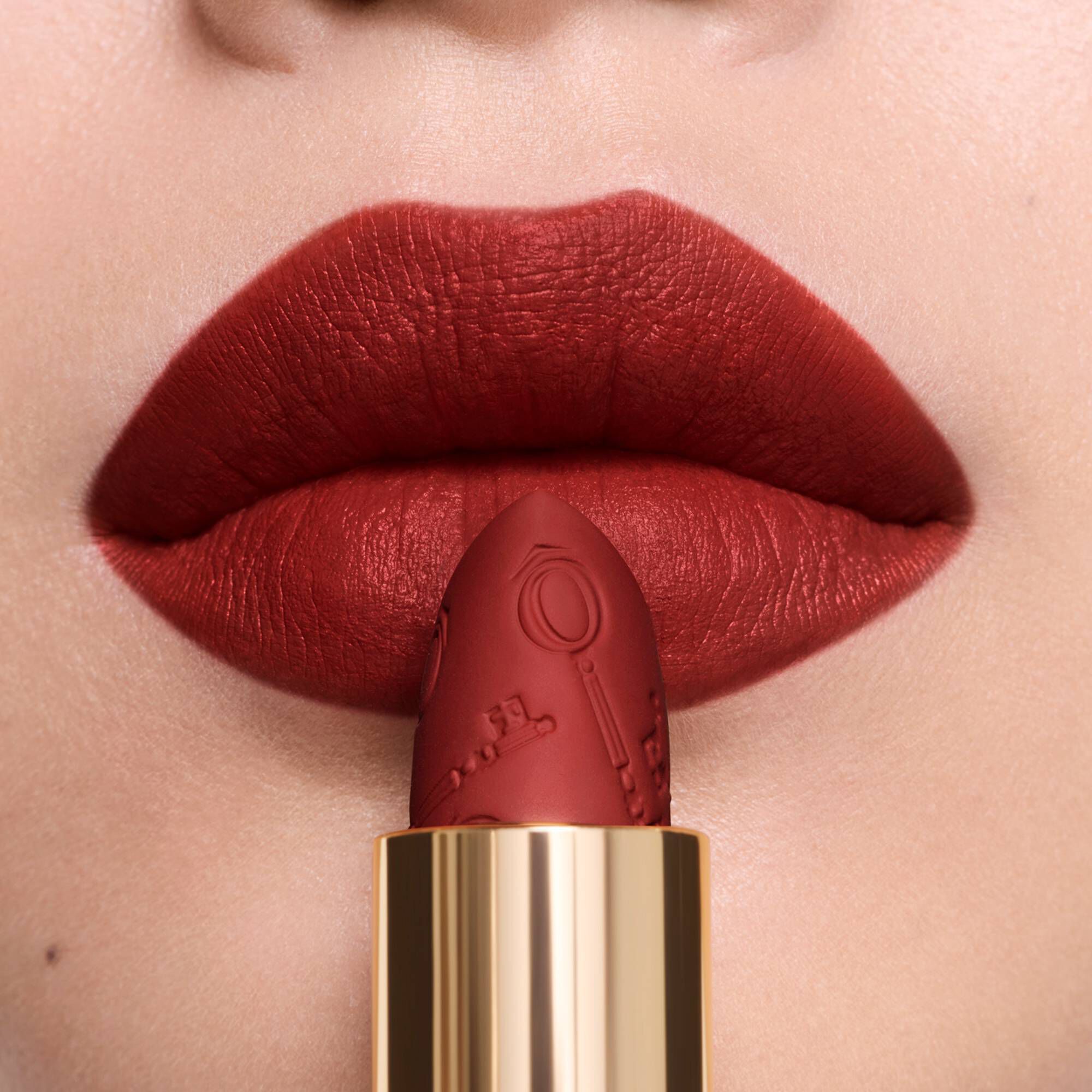A close-up of warm matte lipstick on lips, beside its matching engraved lipstick bullet.  