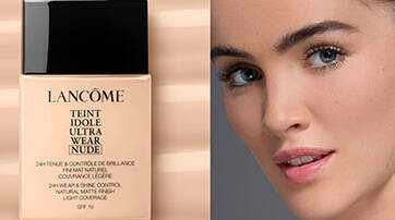 A close-up of a model's face next to a bottle of Lancome Teint Idole Ultra Wear Nude foundation, set against a neutral background with fluid beige tones.
