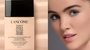 A close-up of a model's face next to a bottle of Lancome Teint Idole Ultra Wear Nude foundation, set against a neutral background with fluid beige tones.