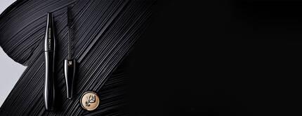 A sleek black mascara tube and wand are elegantly placed on a textured black background, with a gold logo visible nearby.