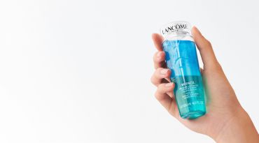 A hand holding a bottle of Lancome skincare product with a blue and turquoise liquid inside, against a plain white background.