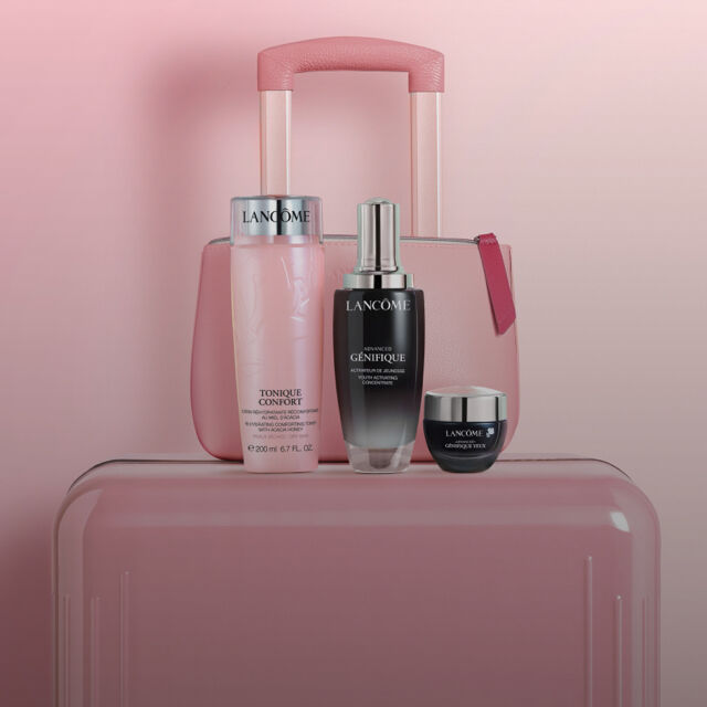 A stylish pink suitcase holds three cosmetics bottles, two taller ones and a small cream jar, against a soft pink gradient background.