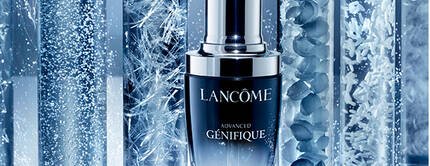 A bottle of Lancome Advanced Genifique serum surrounded by test tubes containing various textures and bubbles, set against a gradient blue background.