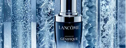 A bottle of Lancome Advanced Genifique serum surrounded by test tubes containing various textures and bubbles, set against a gradient blue background.