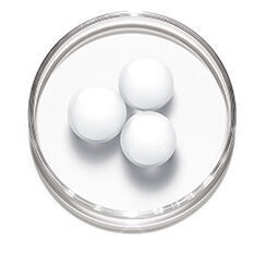 Three white, spherical objects are placed on a white surface inside a clear petri dish.