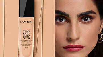A sleek bottle of Lancome Teint Idole Ultra Wear foundation stands against a beige background, next to a close-up of a woman with a flawless complexion, bold eyebrows, and striking red lips.