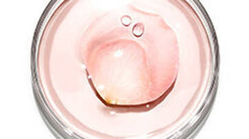 A close-up view of a clear jar containing a pale pink gel with a droplet of liquid resting on top.