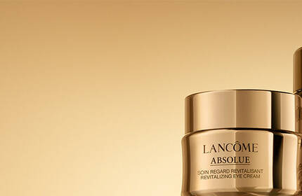 Two luxurious skincare jars from Lancome's Absolue line, featuring a gold gradient background. The jars are elegantly designed with glossy gold lids and labels.