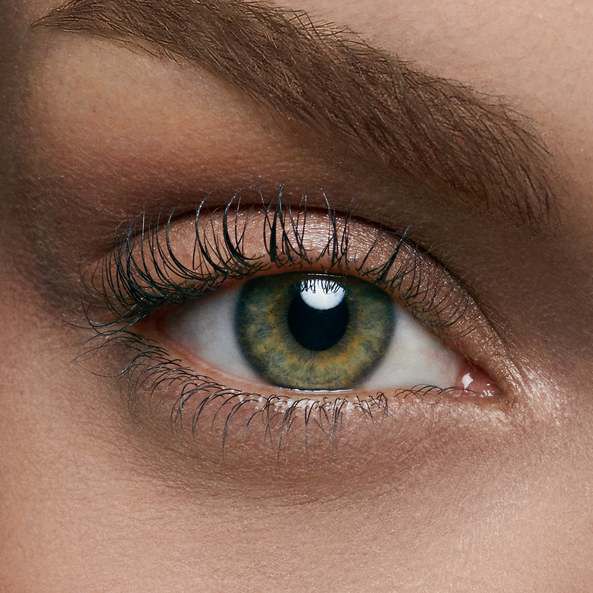 Close-up of a human eye with greenish-brown iris, long eyelashes, and well-groomed eyebrow.