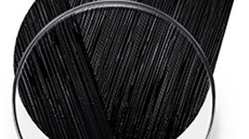 A round dish containing a small golden droplet, with a textured brushstroke of black paint or pigment sweeping across the top.