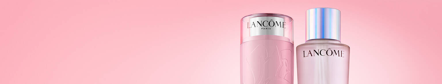 Two Lancome skincare products are displayed against a soft pink background. The left product has a light pink cylindrical bottle with a silver cap, while the right product features a sleek design with a shiny silver lid.