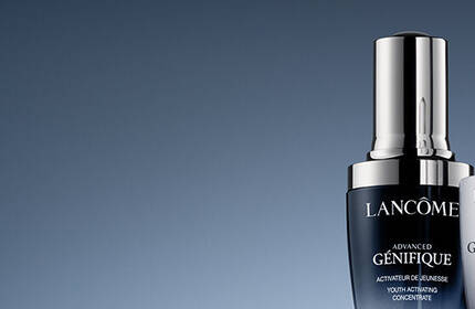 Two luxury skincare serums from Lancome on a gradient background, featuring sleek, modern packaging with silver and black accents. The products include an activating concentrate and an eye treatment.