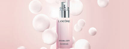 A bottle of Lancome skincare product surrounded by soft, textured bubbles on a light pink background.