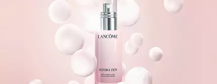 A bottle of Lancome skincare product surrounded by soft, textured bubbles on a light pink background.