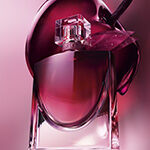Flacon de parfum Lancome Idole entoure de baies rouges, d'une pivoine rose et d'une tranche
            d'agrume sur un fond corail.