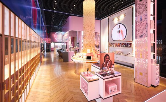 Interieur d'un magasin Lancome lumineux avec des accents roses et dores, presentant des comptoirs d'exposition, un grand lustre cylindrique et des etageres de produits.