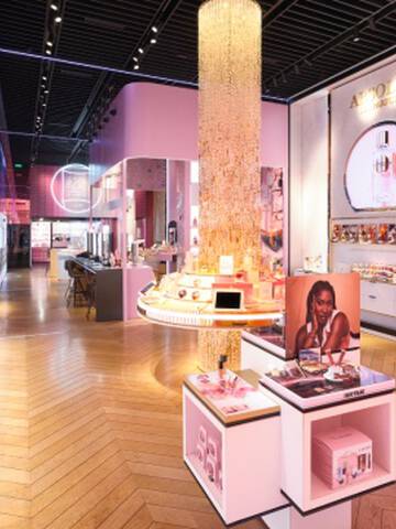 Interieur d'un magasin Lancome lumineux avec des accents roses et dores, presentant des comptoirs d'exposition, un grand lustre cylindrique et des etageres de produits.