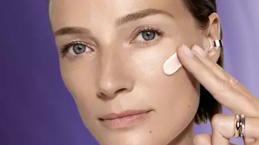 Une personne a la peau claire applique une creme rosee sur sa joue.