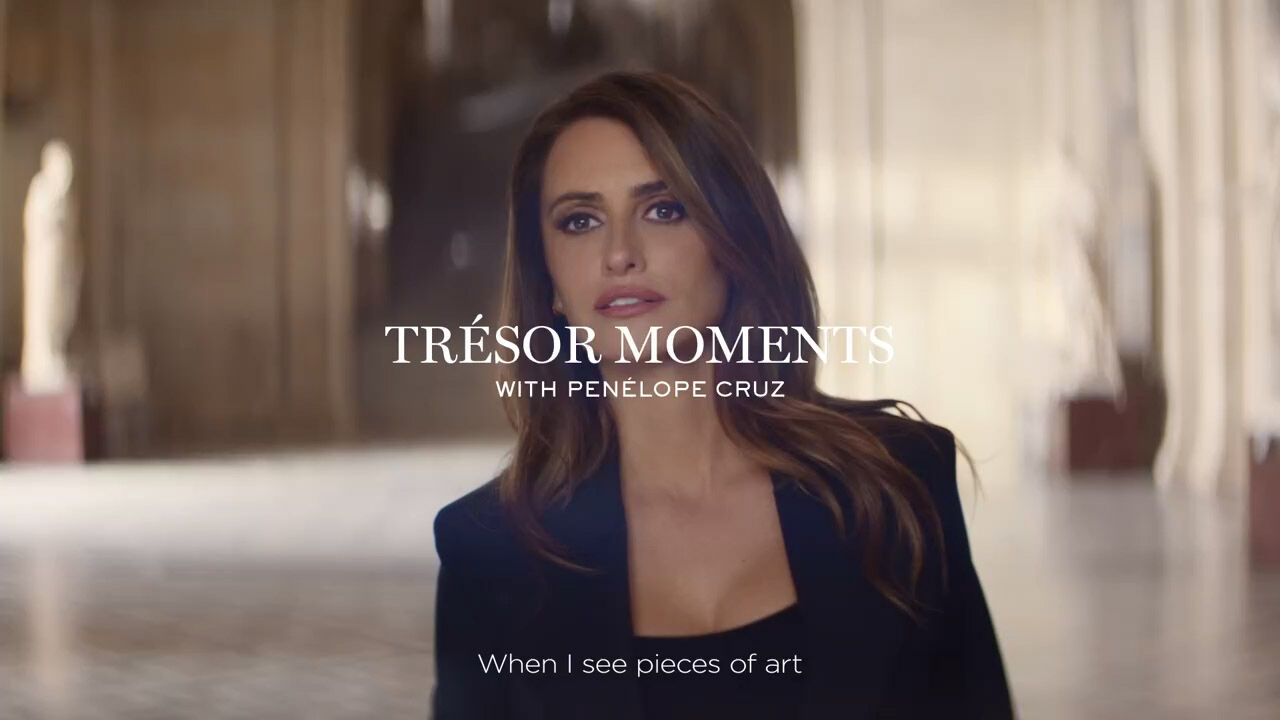 A woman with long, wavy hair is featured in a stylish black outfit, walking through a grand, softly lit interior. The text overlay reads "TRESOR MOMENTS WITH PENELOPE CRUZ," followed by the quote, "When I see pieces of art."