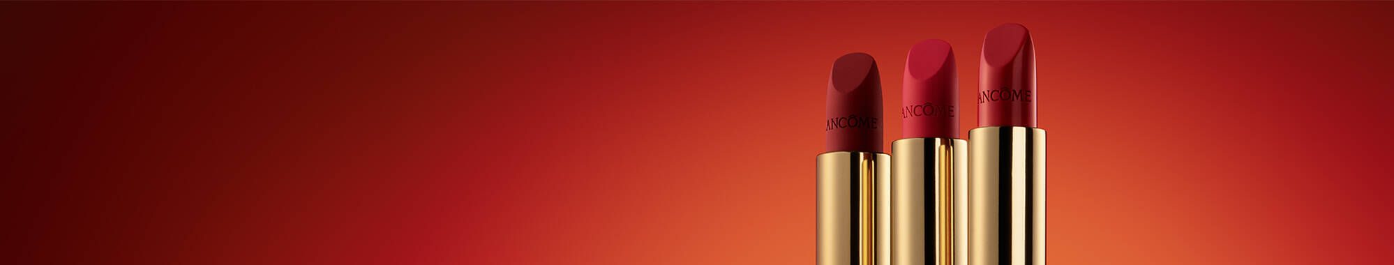 Three red lipsticks with gold packaging are lined up against a gradient red background.