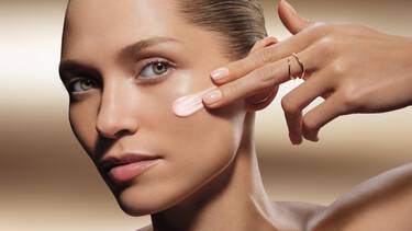 Une personne avec des taches de rousseur applique une creme blanche sur sa joue.