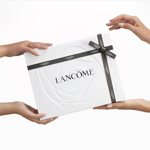Un paquet blanc elegant de Lancome, tenu par deux mains, avec un ruban noir.