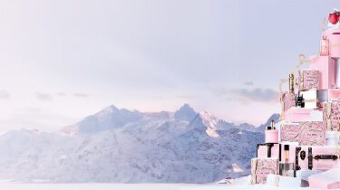 A pink perfume bottle is surrounded by soft pink rose petals against a light background, creating a romantic and elegant atmosphere.