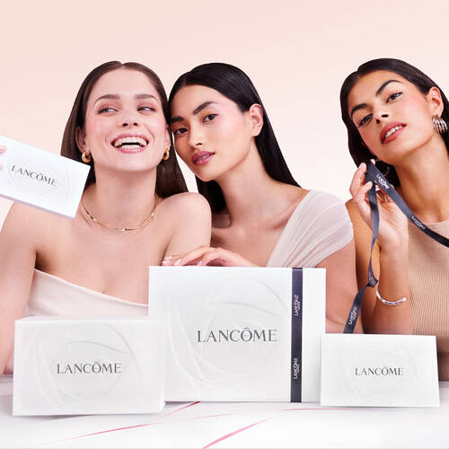 Trois femmes souriantes posent avec des produits de beaute Lancome, tenant des boites et des accessoires.