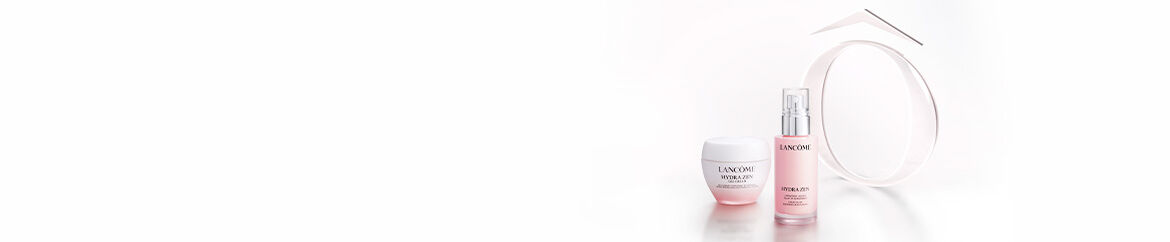 A close-up of two Lancome skincare products on a soft pink background: a jar of Hydra Zen moisturizing cream and a spray bottle of Hydra Zen serum.