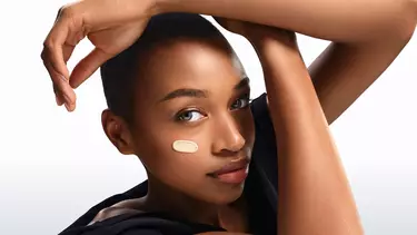 Une personne avec des taches de rousseur applique une creme blanche sur sa joue.