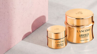 Three luxurious skincare products from Lancome are showcased against a dark background, featuring elegant gold packaging. The items include a serum and two cream jars, highlighting sophistication and beauty.