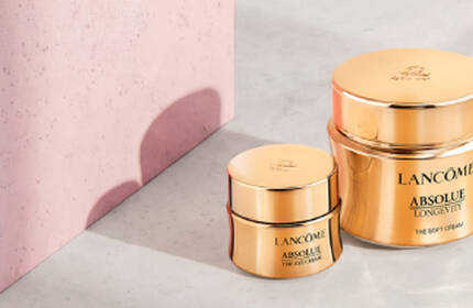 Three luxurious skincare products from Lancome are showcased against a dark background, featuring elegant gold packaging. The items include a serum and two cream jars, highlighting sophistication and beauty.