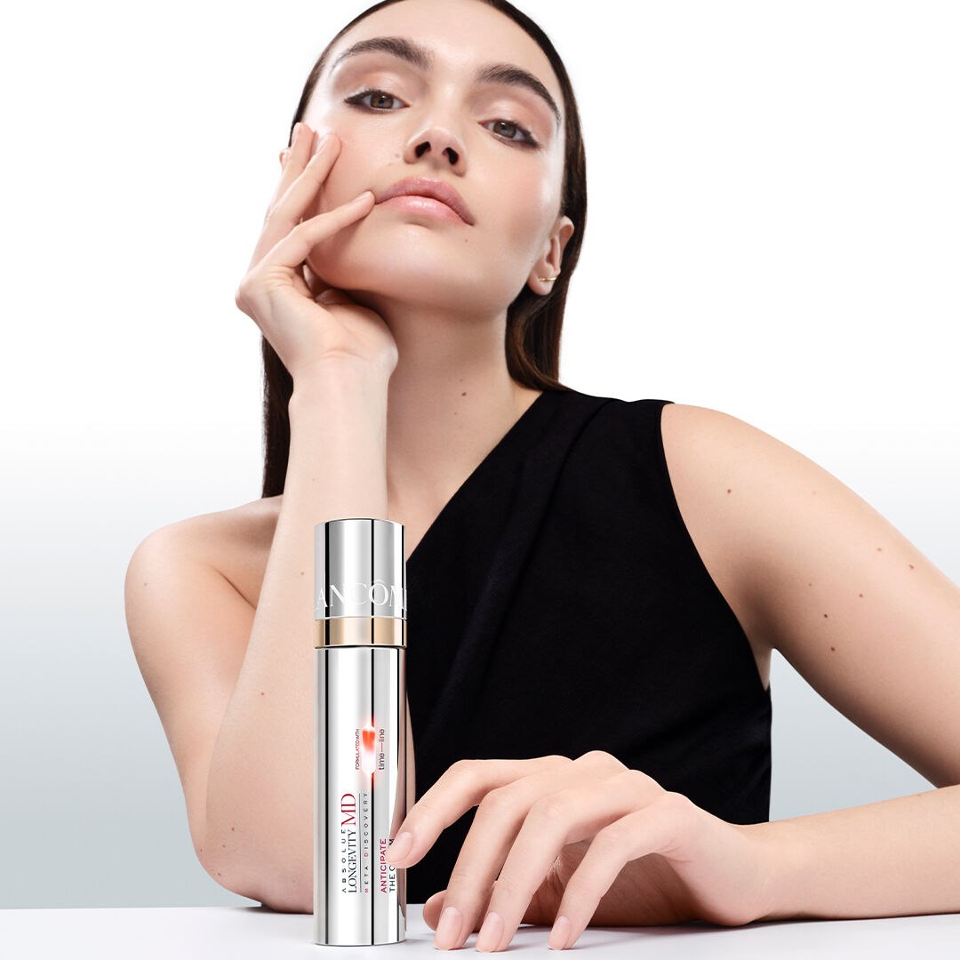 Mannequin a la peau eclatante et lumineuse posant avec le flacon de soin Lancome Absolue Longevity MD sur fond blanc minimaliste