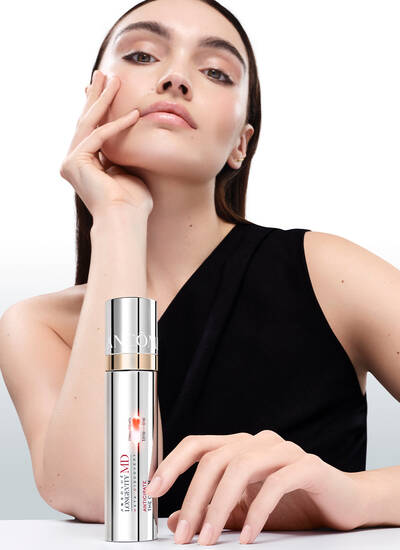 Mannequin a la peau eclatante et lumineuse posant avec le flacon de soin Lancome Absolue Longevity MD sur fond blanc minimaliste