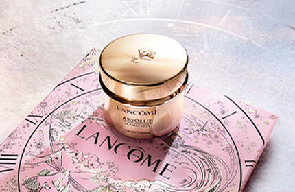 Three luxurious skincare products from Lancome are showcased against a dark background, featuring elegant gold packaging. The items include a serum and two cream jars, highlighting sophistication and beauty.