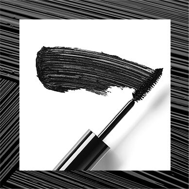 A close-up of a mascara wand coated with black mascara, with a smudge of mascara alongside it on a white background.
