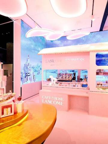 Vue interieure d'un magasin Lancome avec un comptoir sur le theme d'un train rose, une presentation de produits disposes en tour de cadeaux et de grands ecrans numeriques affichant des arriere-plans sceniques.