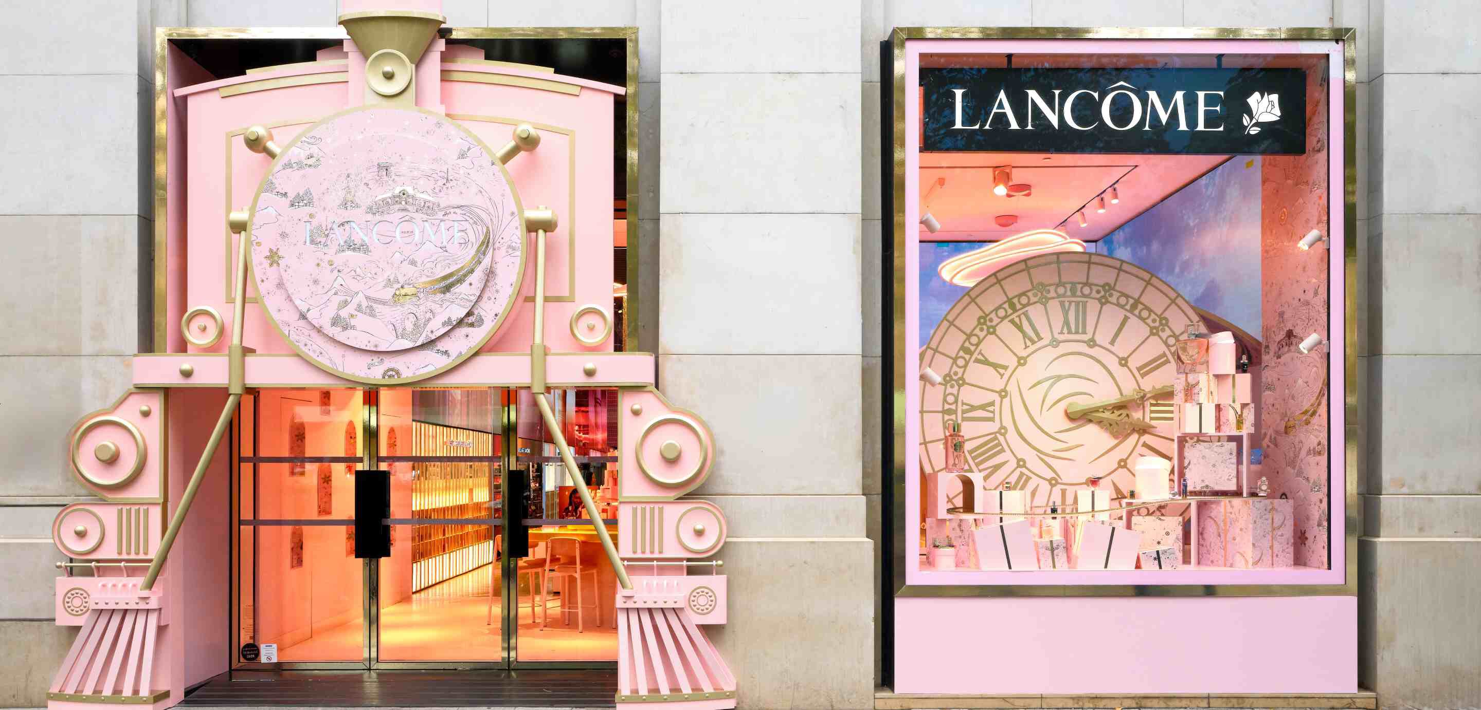 Facade d'un magasin Lancome avec une entree en forme de train rose et une vitrine presentant un grand cadran d'horloge.
