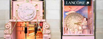 Facade d'un magasin Lancome avec une entree en forme de train rose et une vitrine presentant un grand cadran d'horloge.