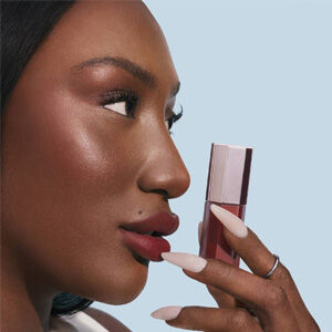 Flacon de parfum Lancome Idole entoure de baies rouges, d'une pivoine rose et d'une tranche
            d'agrume sur un fond corail.