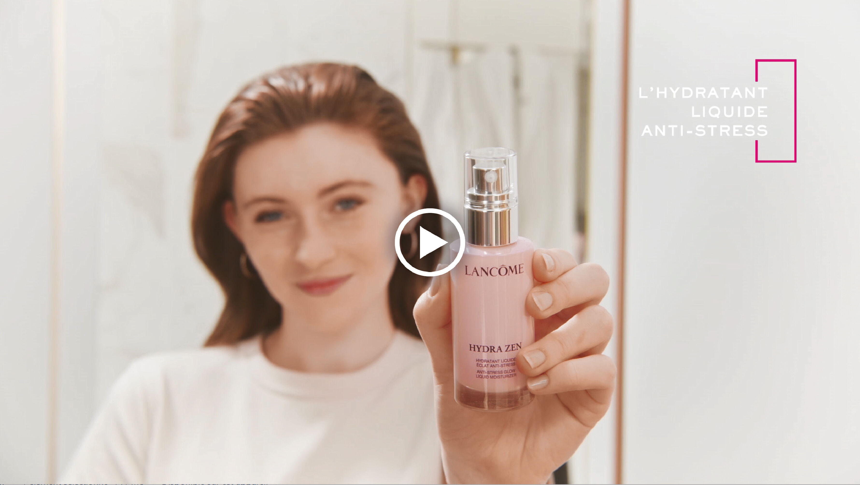 Une femme souriante tient un flacon de l'hydratant liquide anti-stress Hydra Zen de Lancome dans une salle de bain.