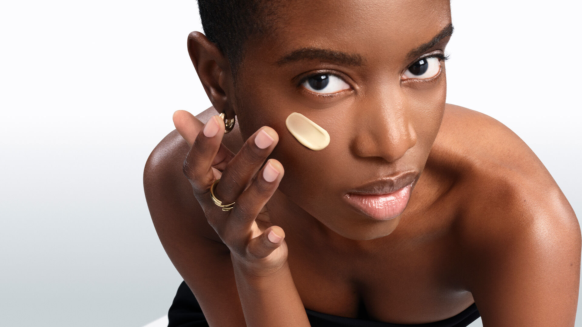 Une personne avec des taches de rousseur applique une creme blanche sur sa joue.