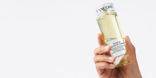 A hand holding a bottle of Lancome skincare product, featuring a clear liquid inside and a label with product details.