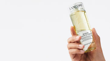 A hand holding a bottle of Lancome skincare product, featuring a clear liquid inside and a label with product details.