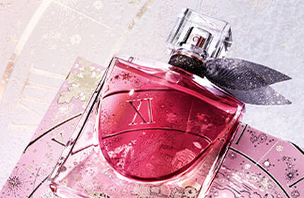 A beautifully arranged gift set featuring a perfume bottle and a tube of lotion, displayed on an intricate dark background with elegant golden designs. Hands gently hold the box, emphasizing the luxurious presentation.