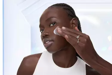 Une personne a la peau foncee applique une creme blanche sur sa joue.