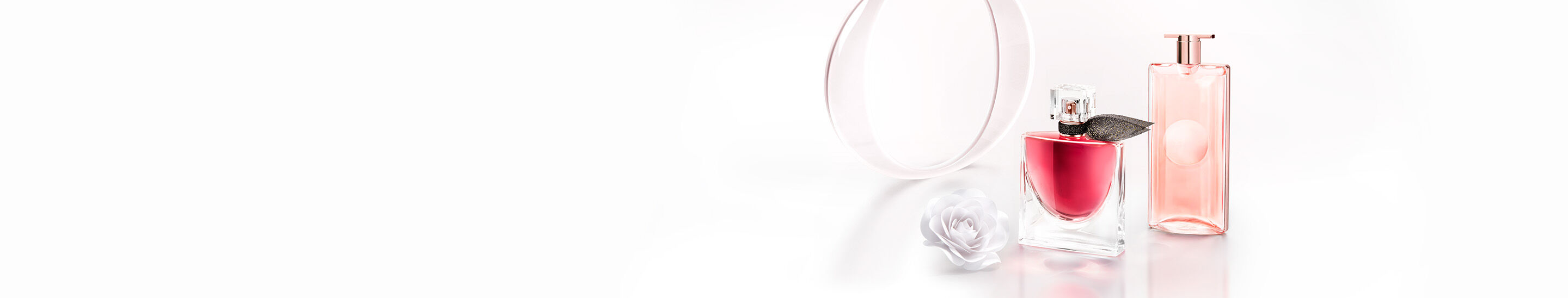 Two elegant perfume bottles are displayed alongside a white flower and a circular mirror, set against a clean white background. One bottle features a pink liquid and a decorative leaf, while the other is a sleek, transparent pink design.