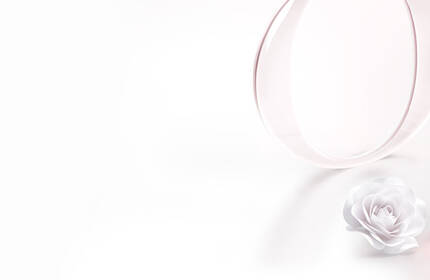Two elegant perfume bottles are displayed alongside a white flower and a circular mirror, set against a clean white background. One bottle features a pink liquid and a decorative leaf, while the other is a sleek, transparent pink design.