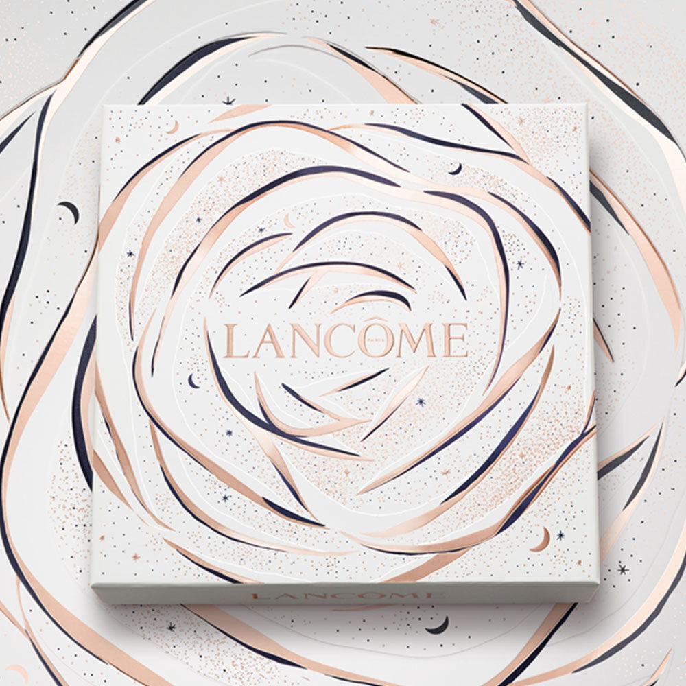 A decorative box featuring a rose design with swirling lines in gold and white, prominently displaying the word "LANCOME." The background has a subtle starry theme.